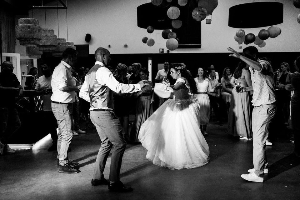 Zwart-witfoto van mensen die dansen op een feest, met ballonnen en gasten op de achtergrond.