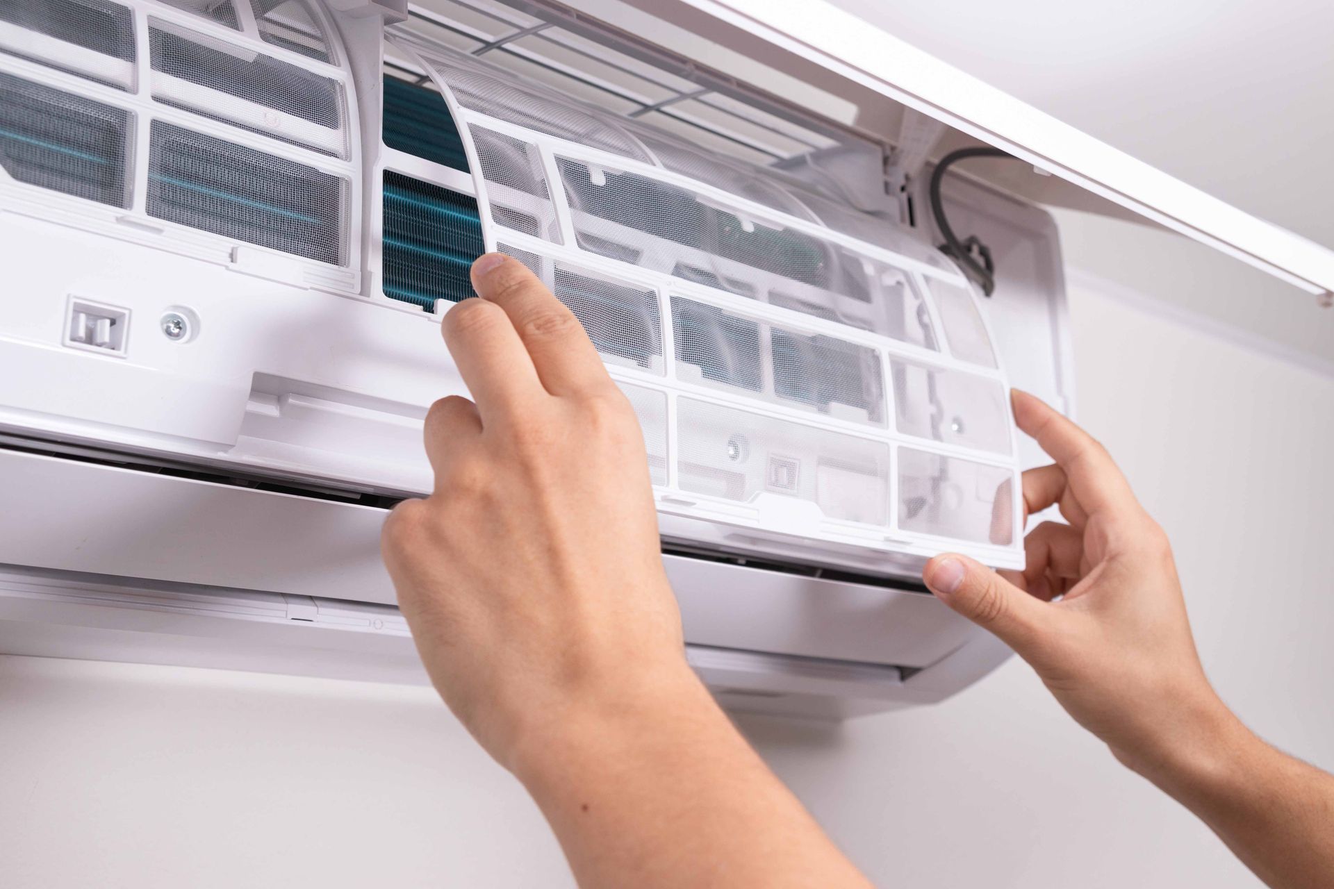 Hands removing air filter from a wall-mounted air conditioning unit. Hands removing air filter from a wall-mounted air conditioning unit.