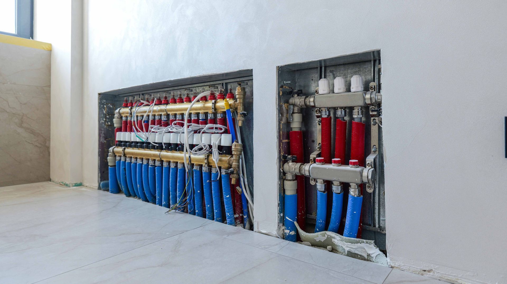 Two recessed wall panels with red and blue pipes and valves for a radiant heating system. Two recessed wall panels with red and blue pipes and valves for a radiant heating system.