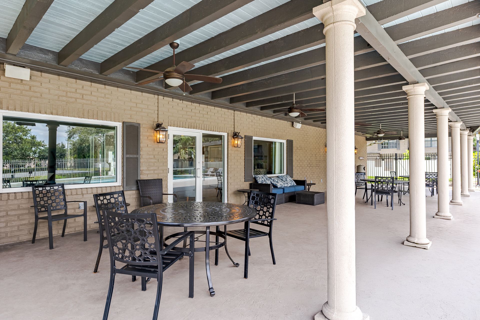 A spacious, covered outdoor patio featuring decorative columns, a round metal table with chairs, and a couch at Veridian of Melbourne Townhome Apartments in Melbourne, FL.