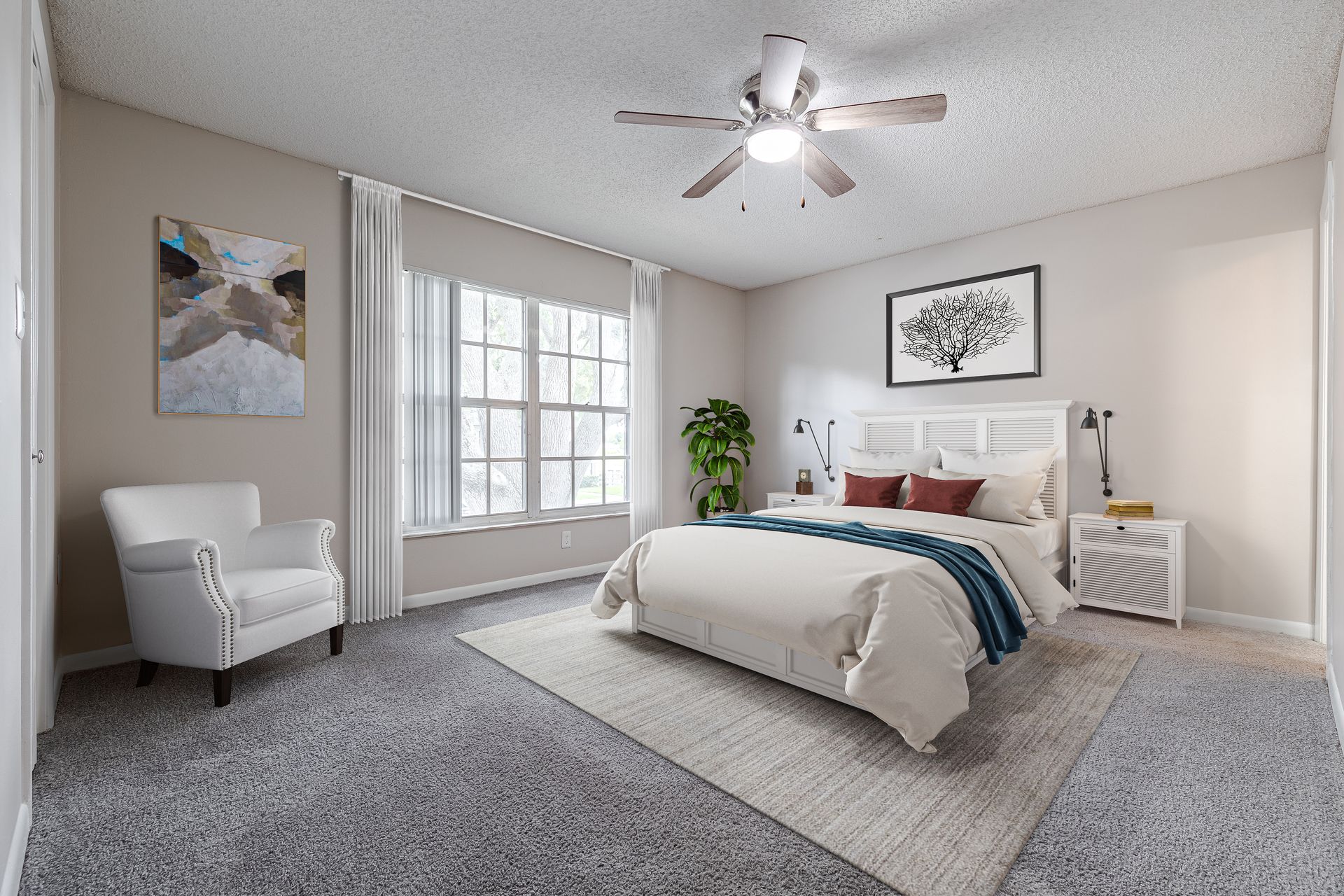 A bedroom with a queen bed, grey carpet, a white armchair, large windows, and a ceiling fan in a neutral-toned room at Veridian of Melbourne Townhome Apartments in Melbourne, FL.