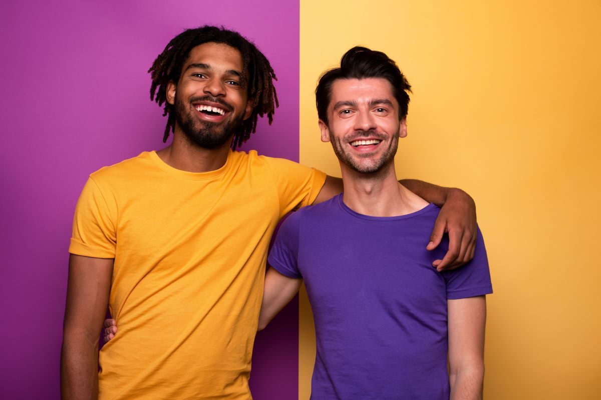 Two men are hugging each other in front of a yellow and purple wall.