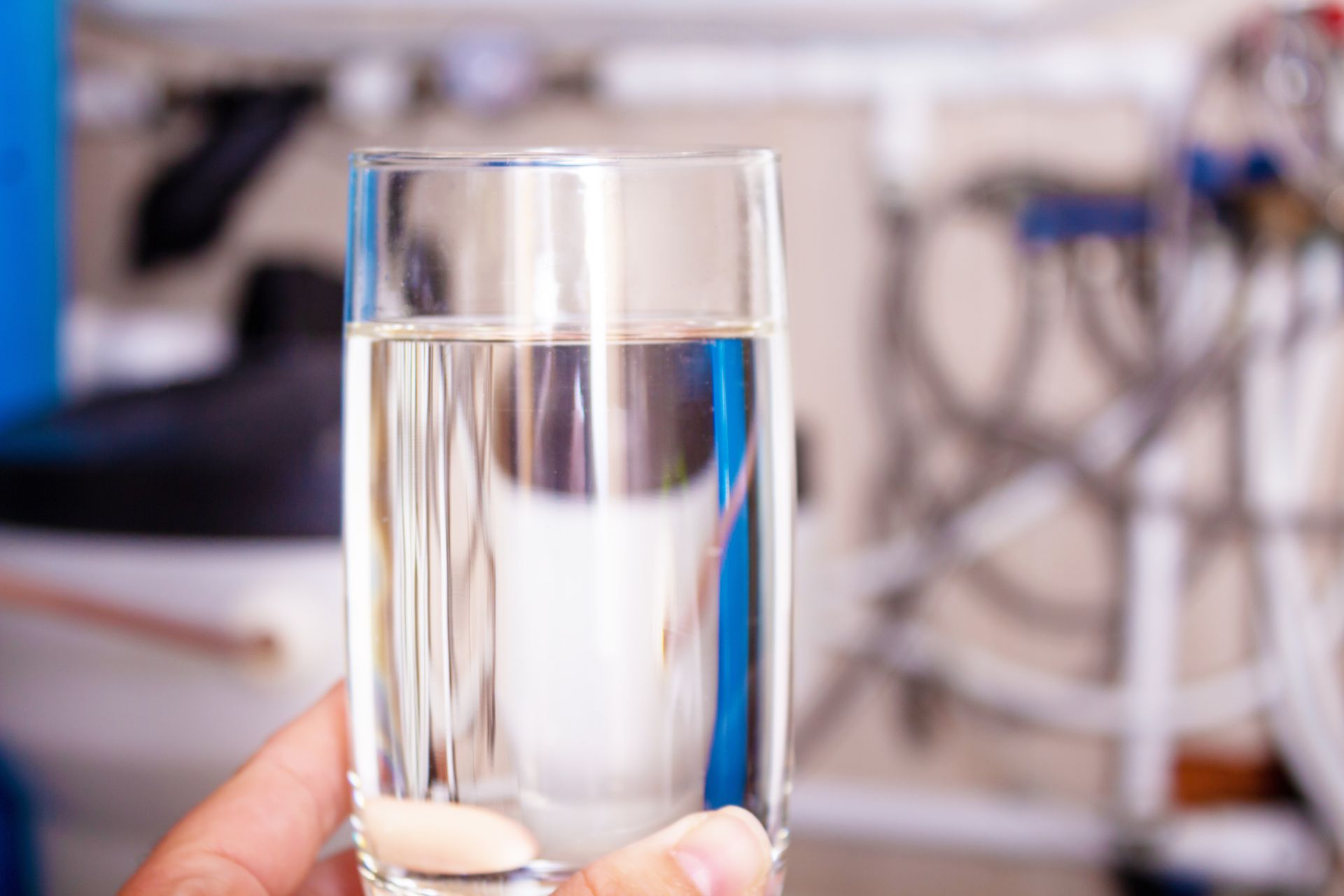 Hand holding a clear glass of filtered water with home water treatment equipment blurred behind. Hand holding a clear glass of filtered water with home water treatment equipment blurred behind.