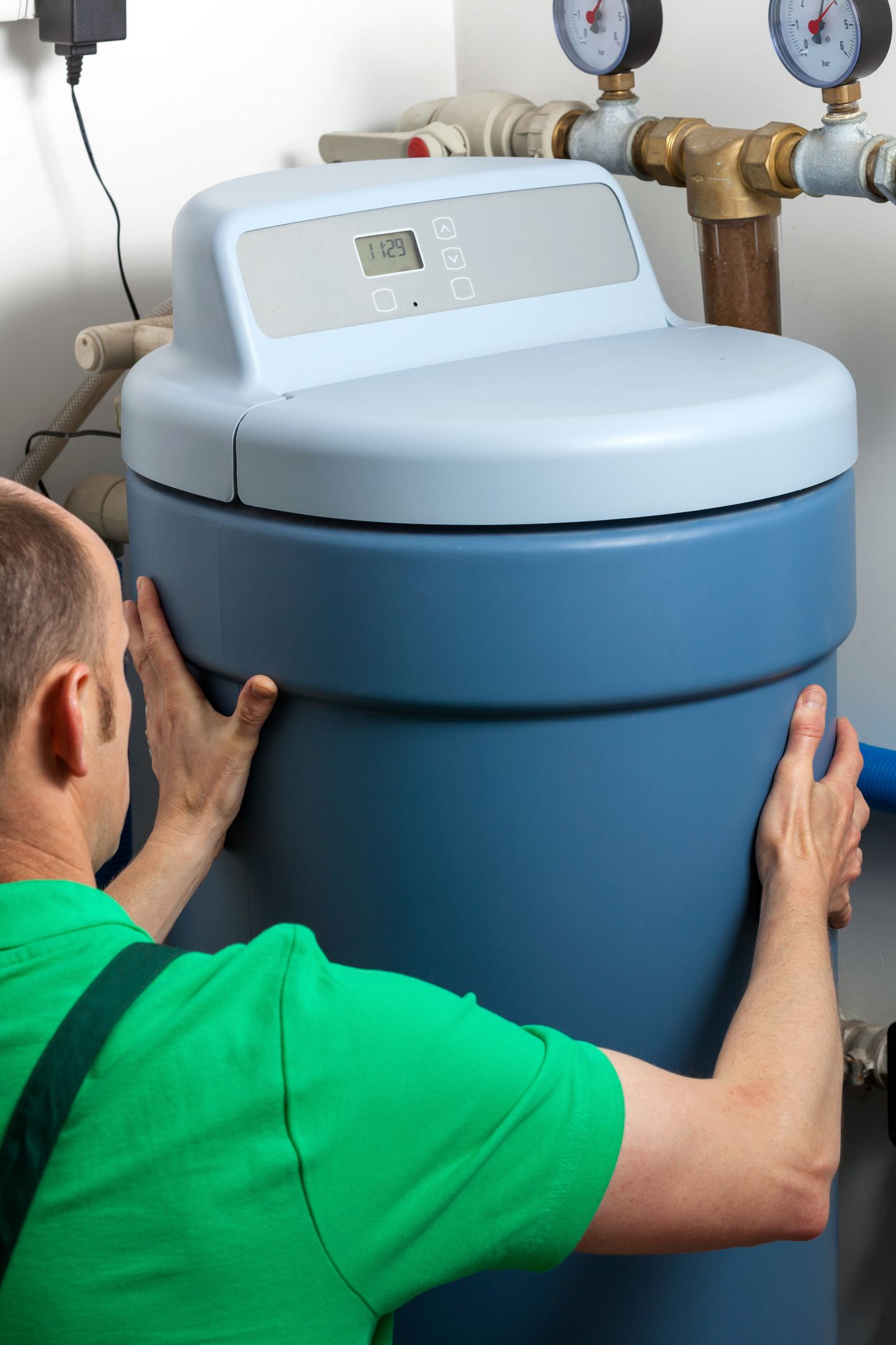 Softener in boiler room water treatment system A man in a green shirt is working on a water softener.