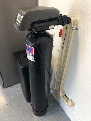 A black water softener is sitting next to a white wall.