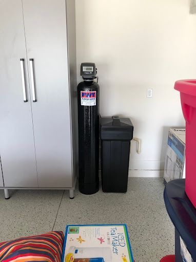 A water softener is sitting next to a trash can in a garage.