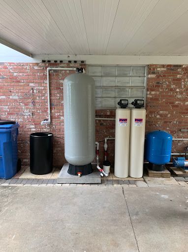 A couple of water tanks are sitting under a brick wall.