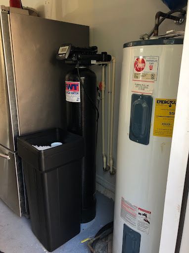 A water filter and a water heater are in a room next to a refrigerator.