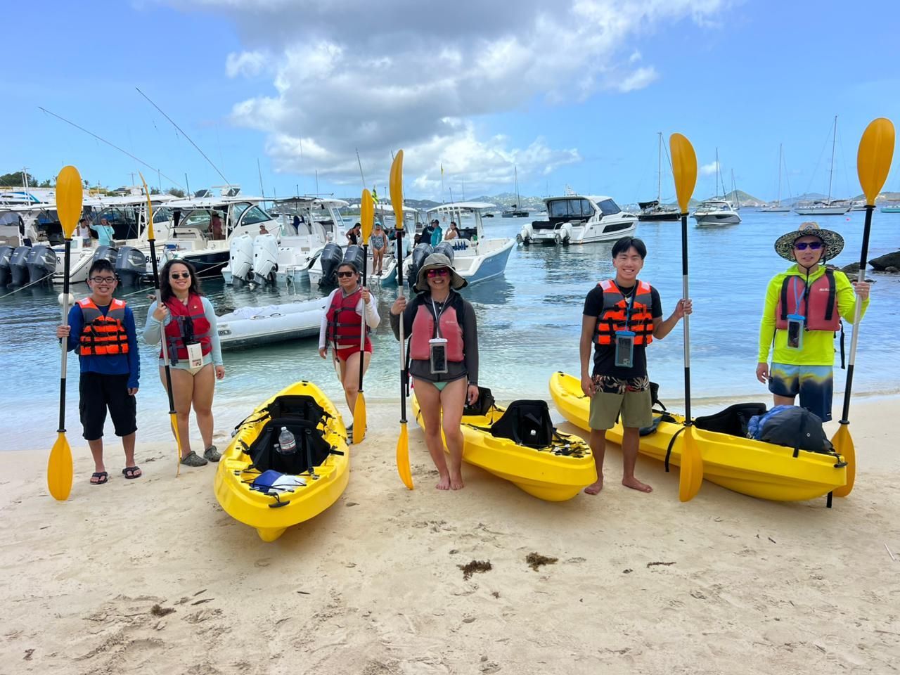 A group of people are standing next to kayaks on a beach.