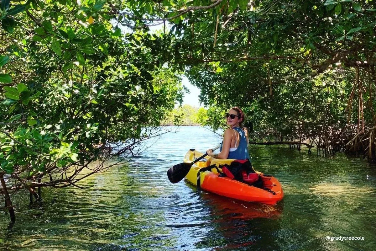 A woman is riding a kayak down a river surrounded by trees.