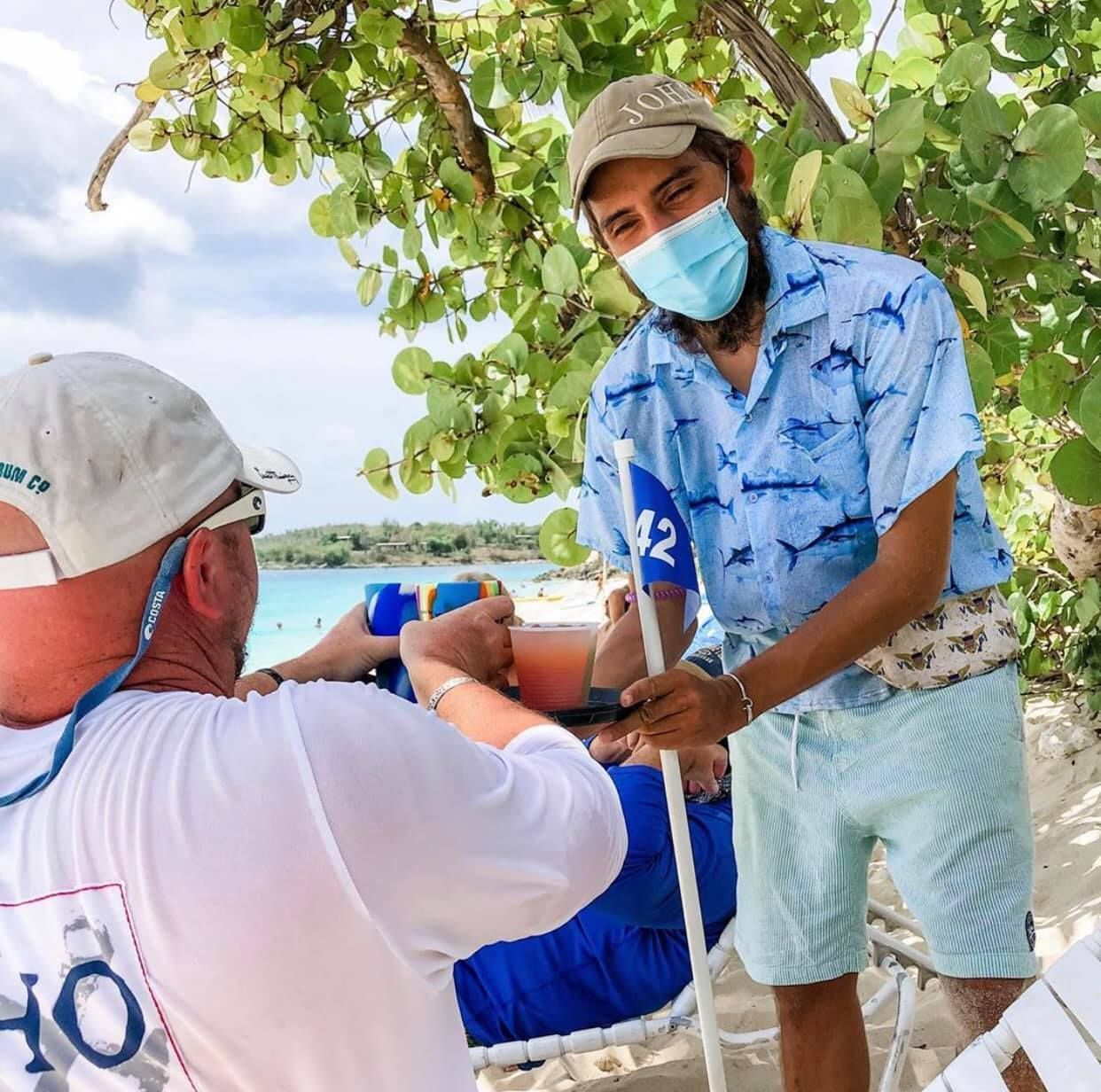 A man wearing a mask is talking to another man on the beach