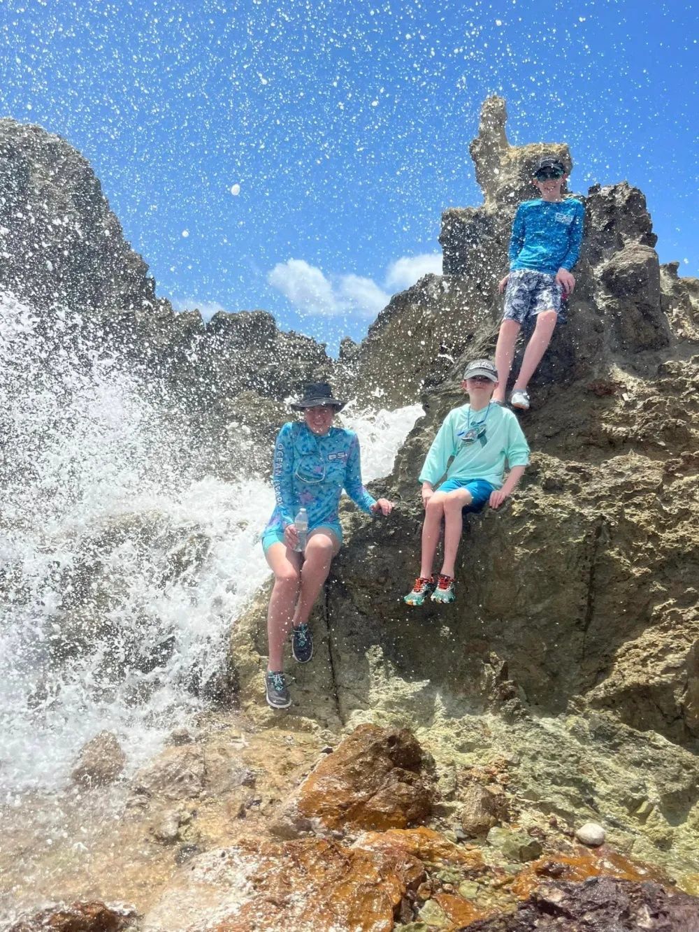 Three people are sitting on rocks near a waterfall.