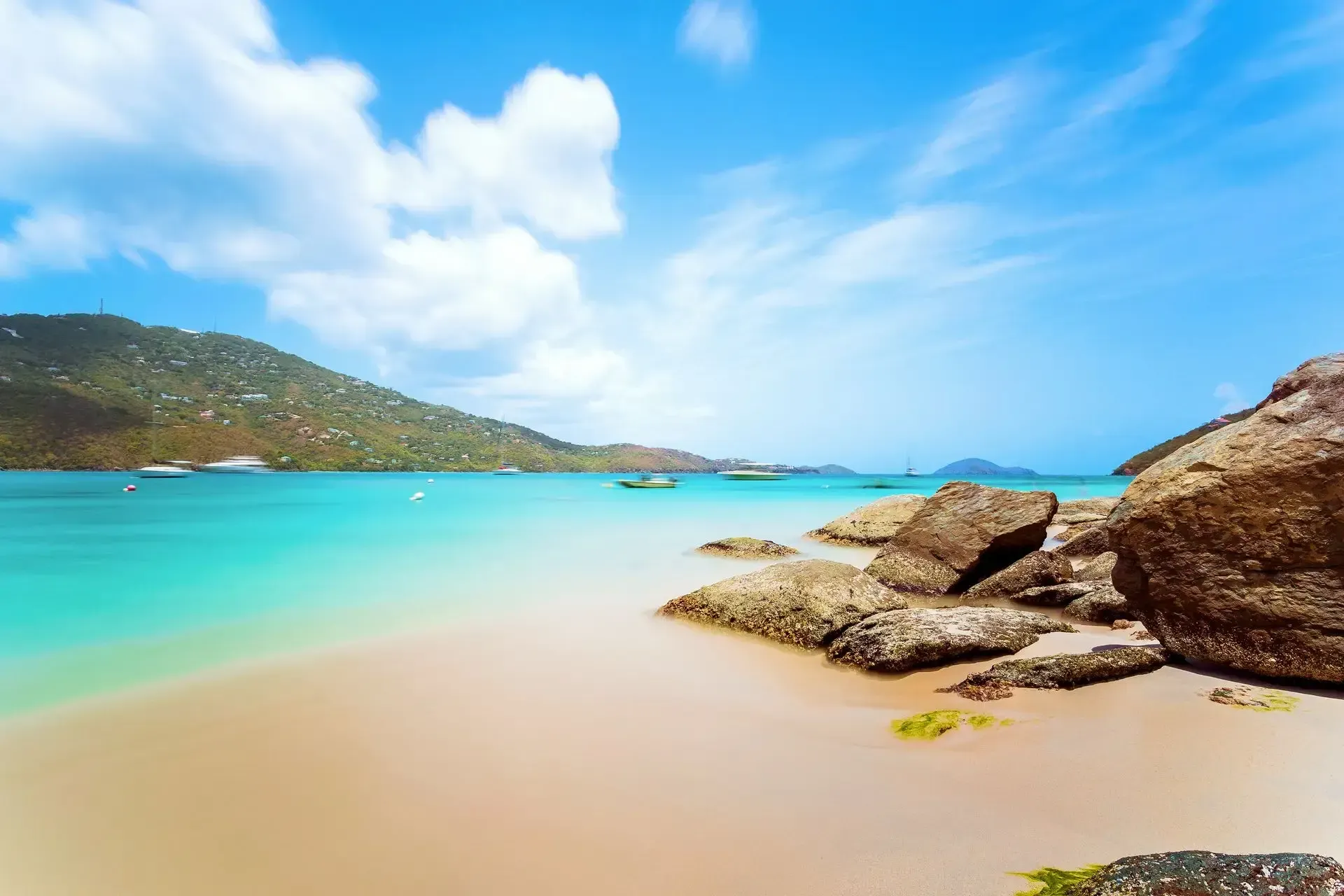 A beach with rocks and boats in the water on a sunny day.