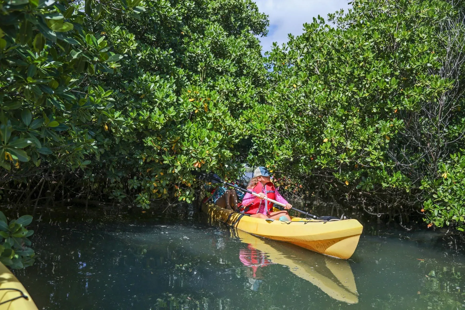 A woman is paddling a yellow kayak in a river surrounded by trees