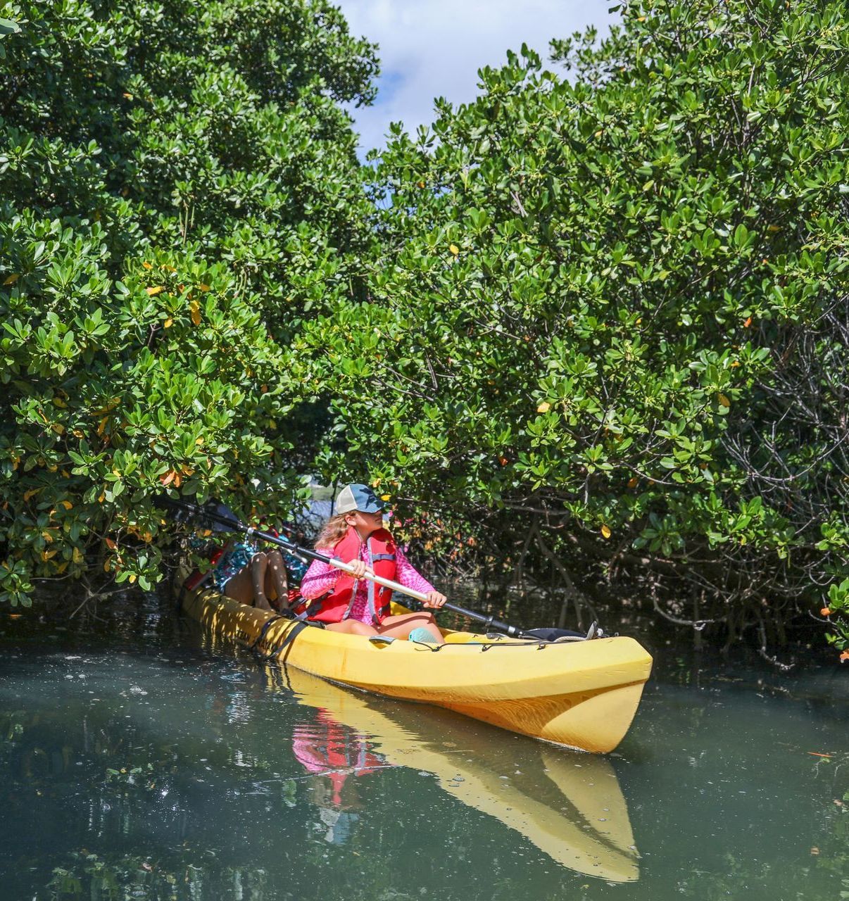 A woman is paddling a yellow kayak in a river surrounded by trees