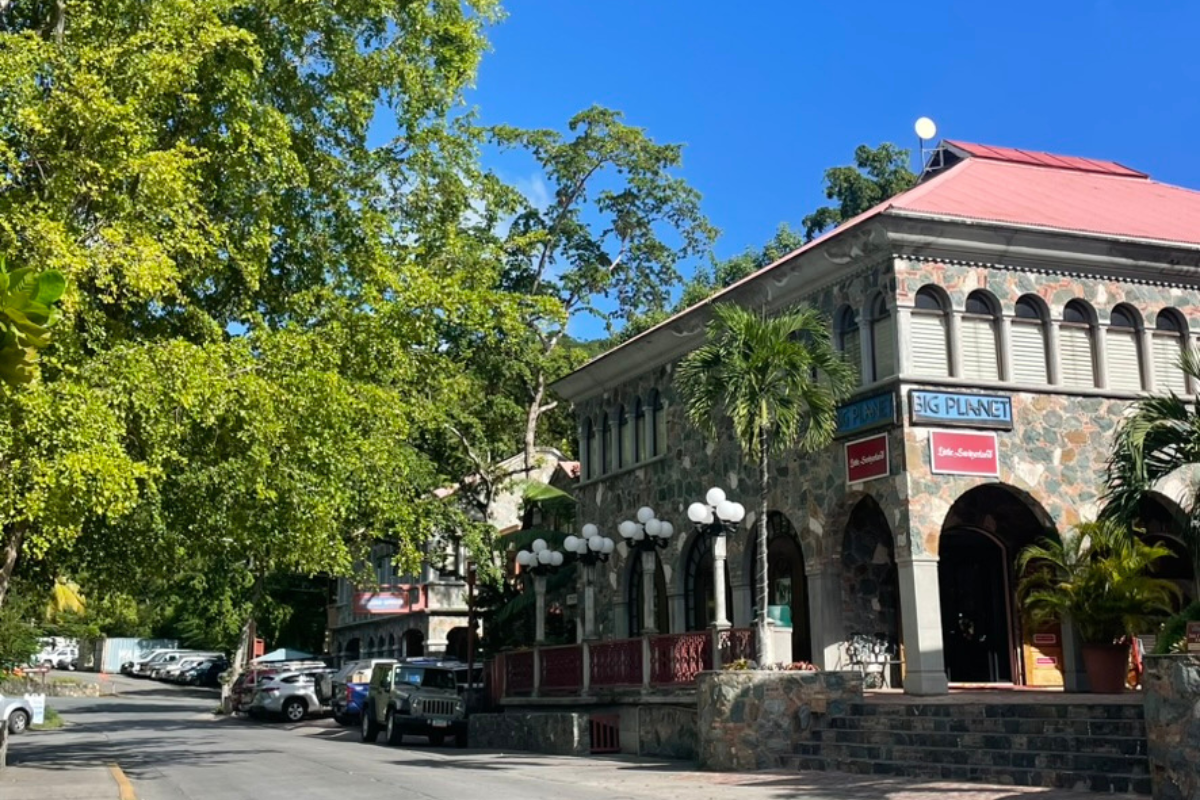 Stone building with arched entrance, street scene, cars, blue sky, green trees.