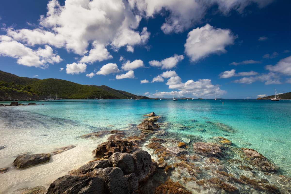 A rocky shoreline with a turquoise ocean and mountains in the background