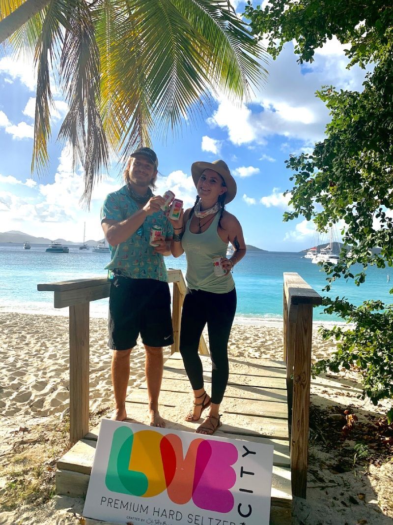 A man and a woman are standing on a beach holding a sign that says love city.
