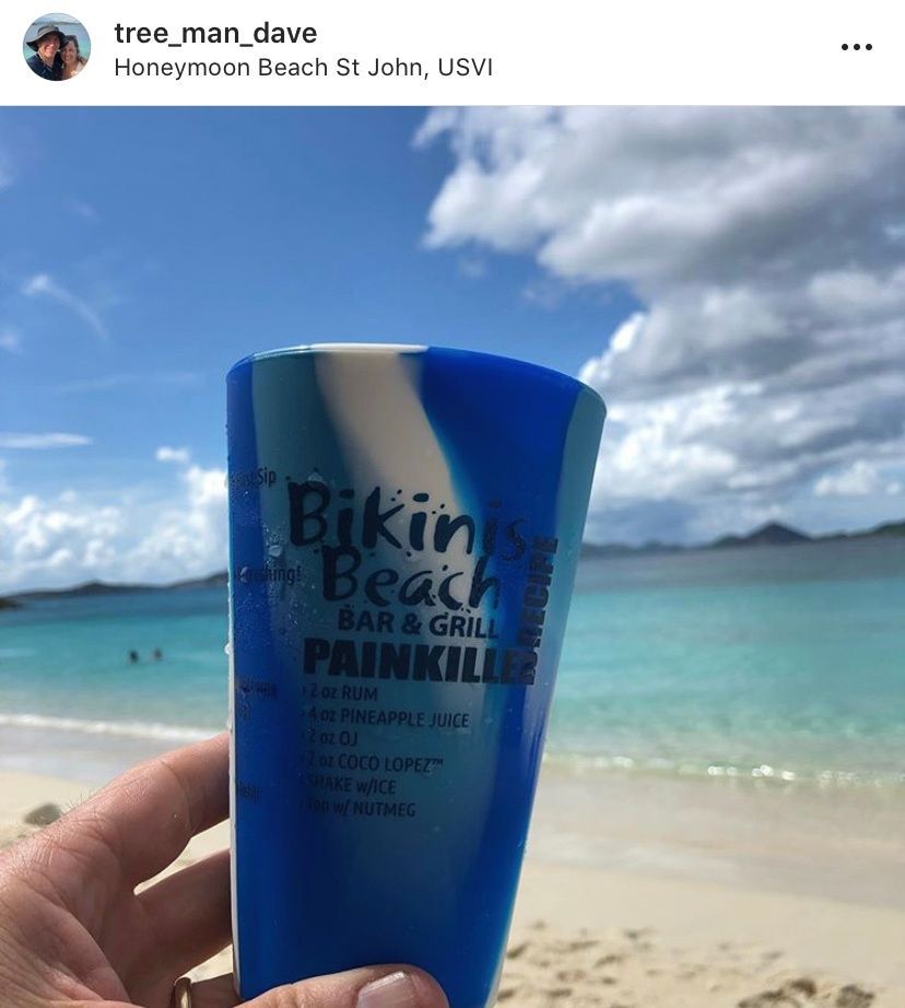A person is holding a blue cup that says bikini beach bar & grill painkiller