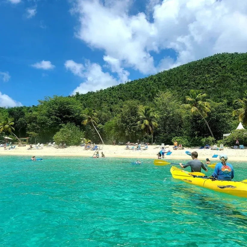 Two people are in a yellow kayak in the ocean near a beach.