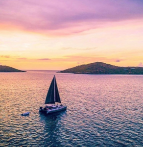 An aerial view of a sailboat in the ocean at sunset.