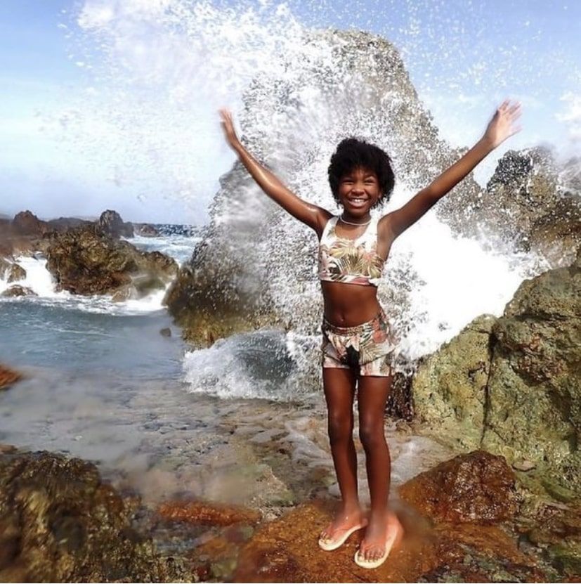 A young girl is standing in front of a wave with her arms outstretched