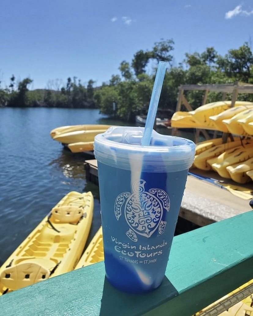 A blue cup with a straw is sitting on a railing near kayaks