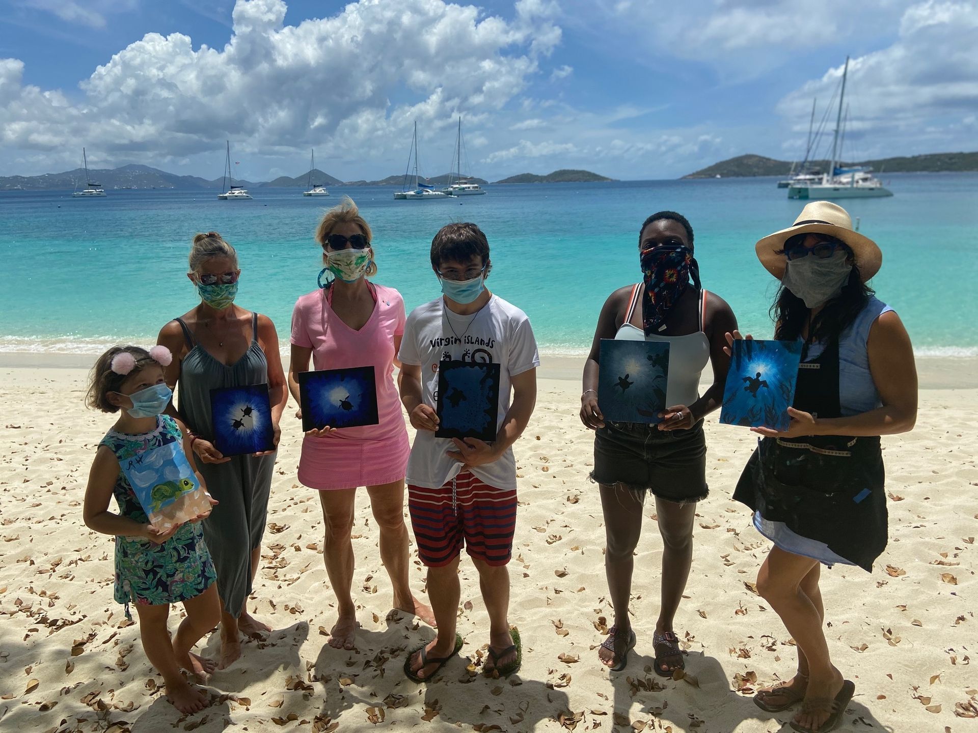 A group of people wearing face masks are standing on a beach holding books.