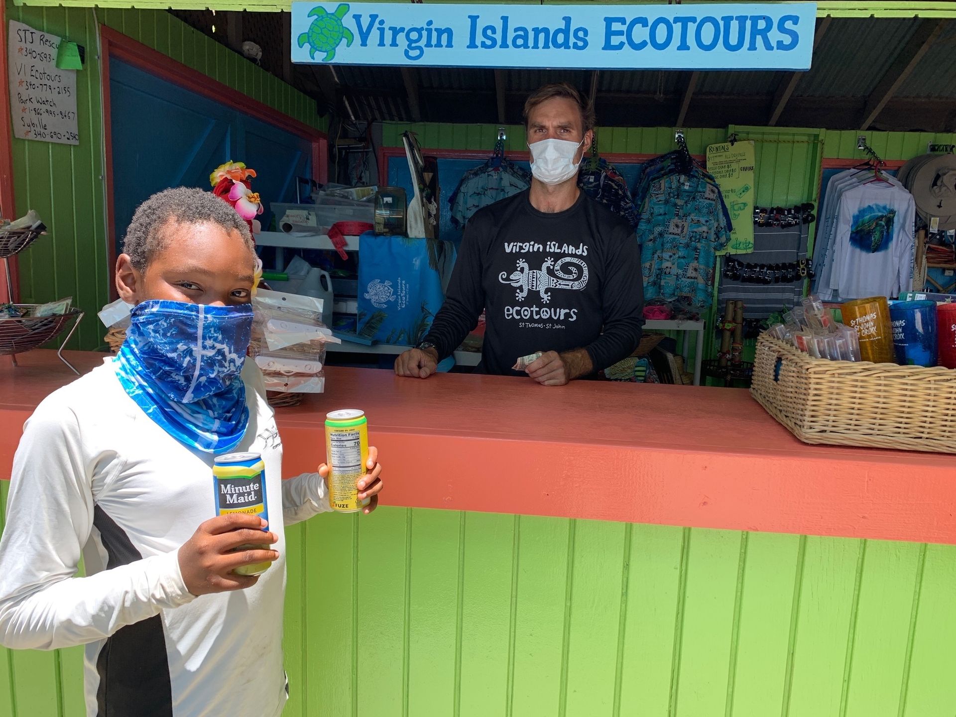 A man and a woman wearing face masks are standing in front of a virgin islands ecotours store.
