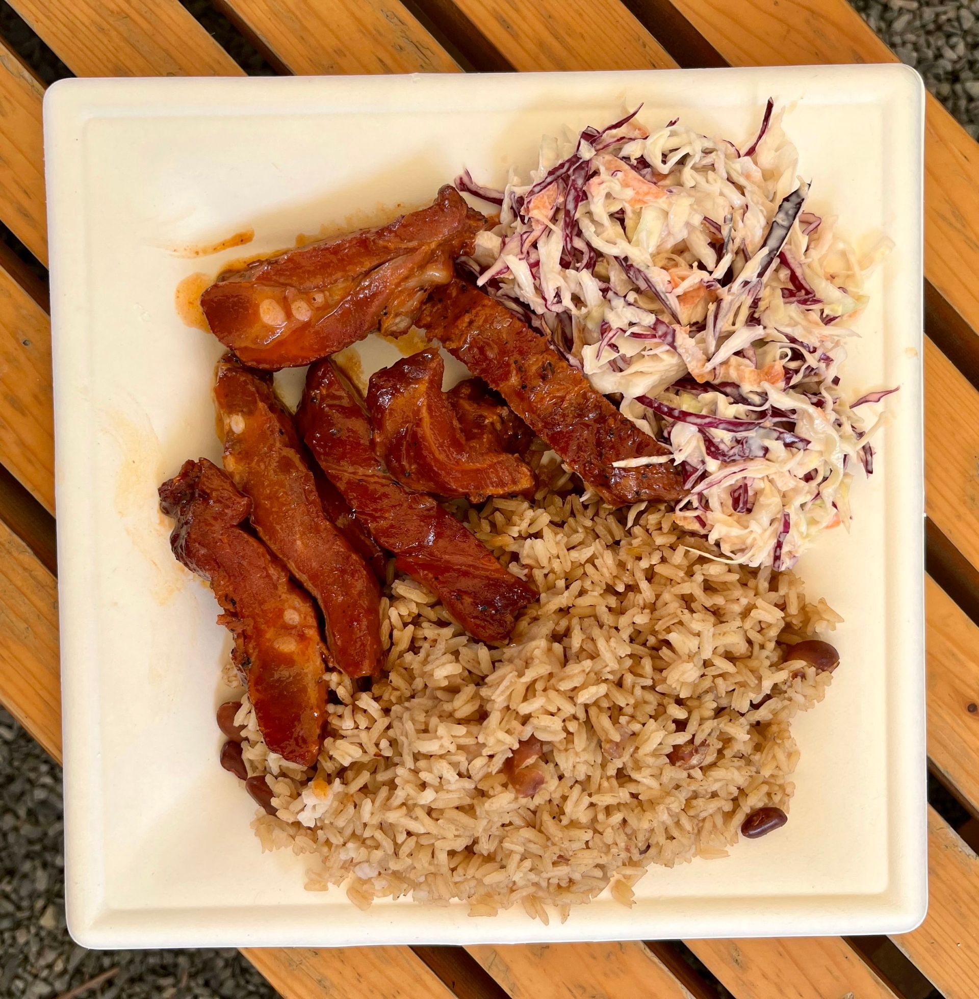 A plate of food with rice and coleslaw on a wooden table