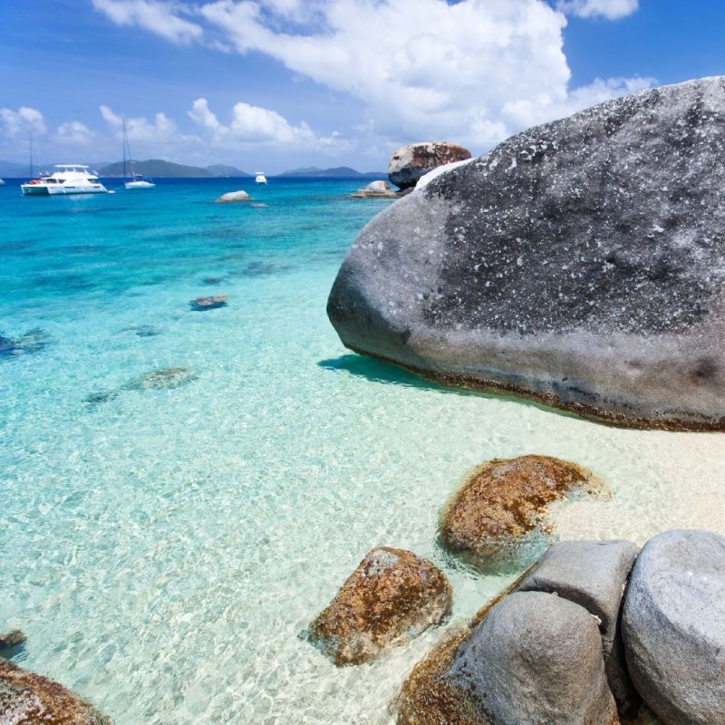 A large rock sits on the shore of a tropical beach