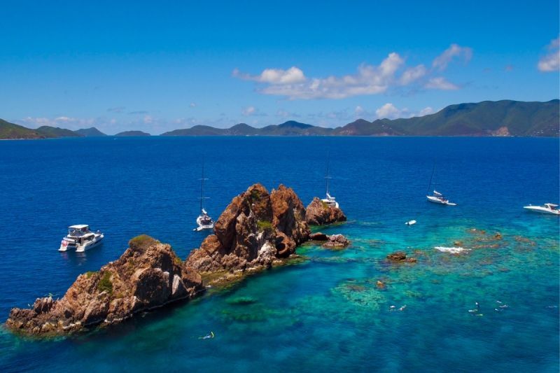 An aerial view of a small island in the middle of the ocean with boats in the water.