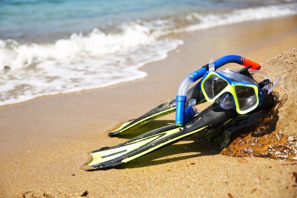 A pair of flippers and a mask are on the beach.