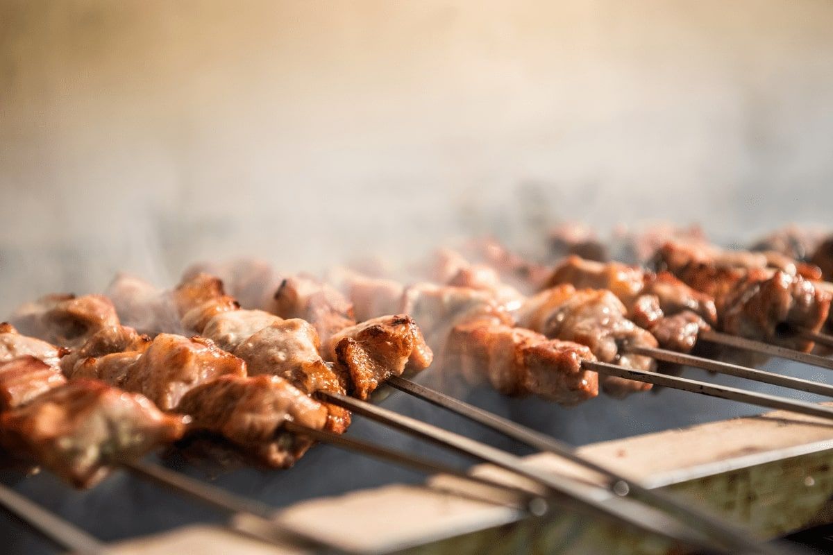 A bunch of meat is being cooked on skewers on a grill.