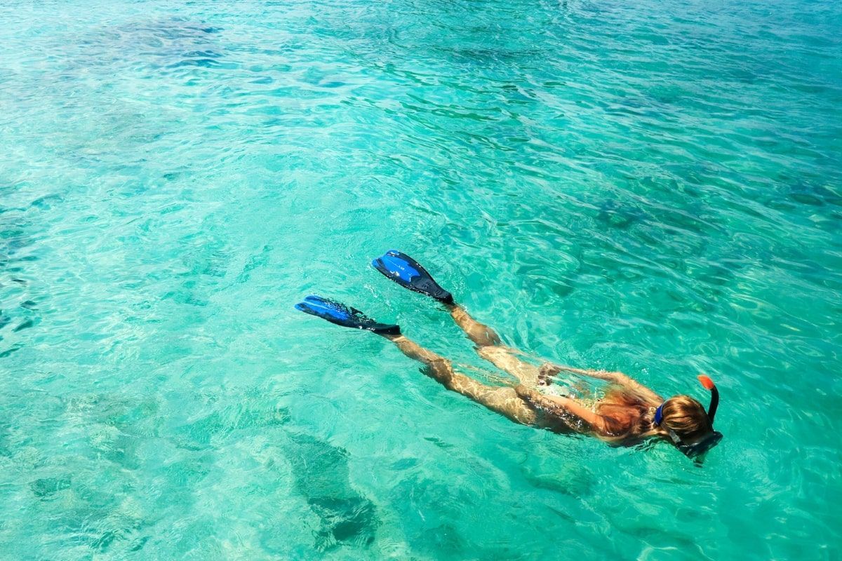 A woman is swimming in the ocean with flippers and a mask on.