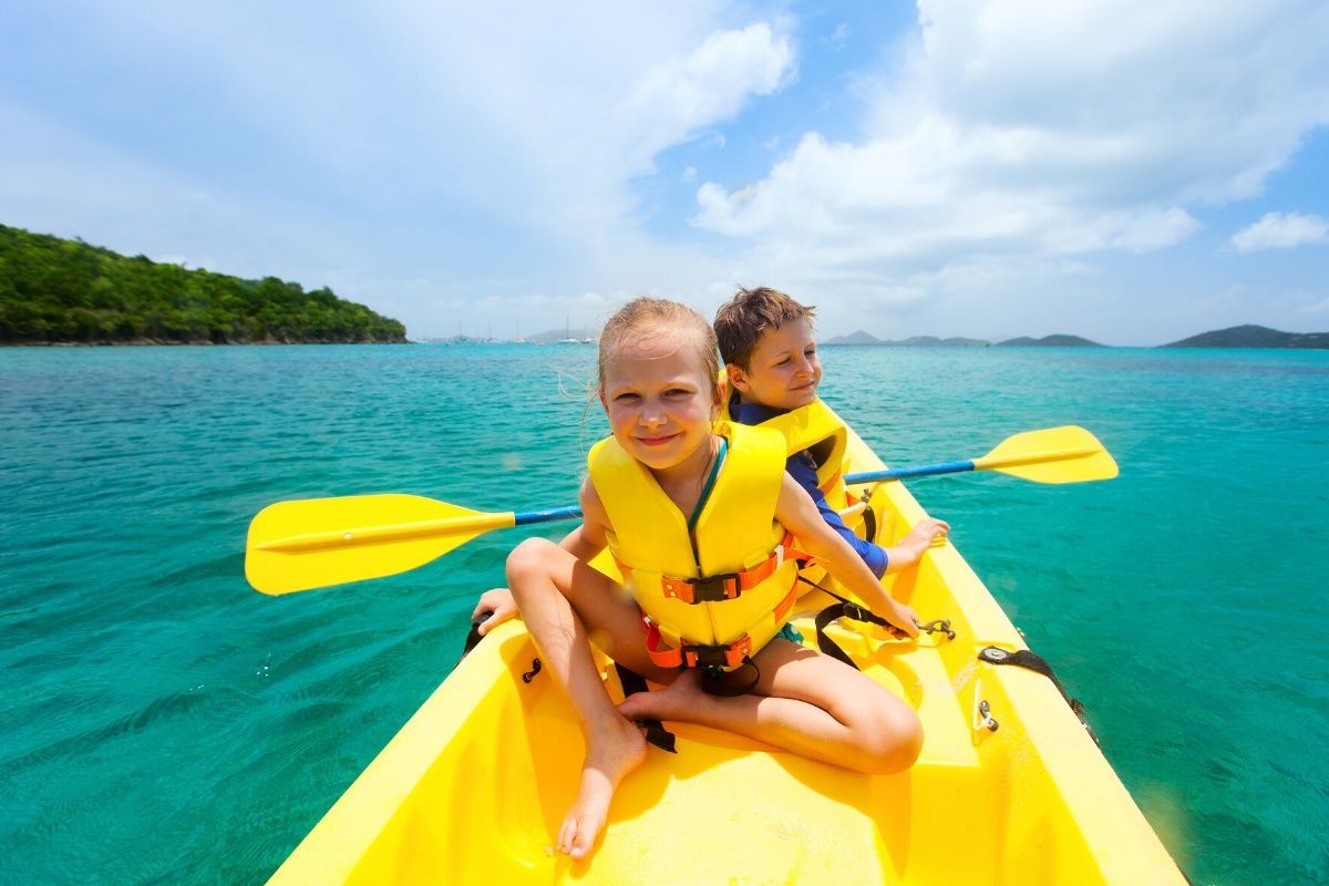 A boy and a girl are sitting in a yellow kayak in the ocean.