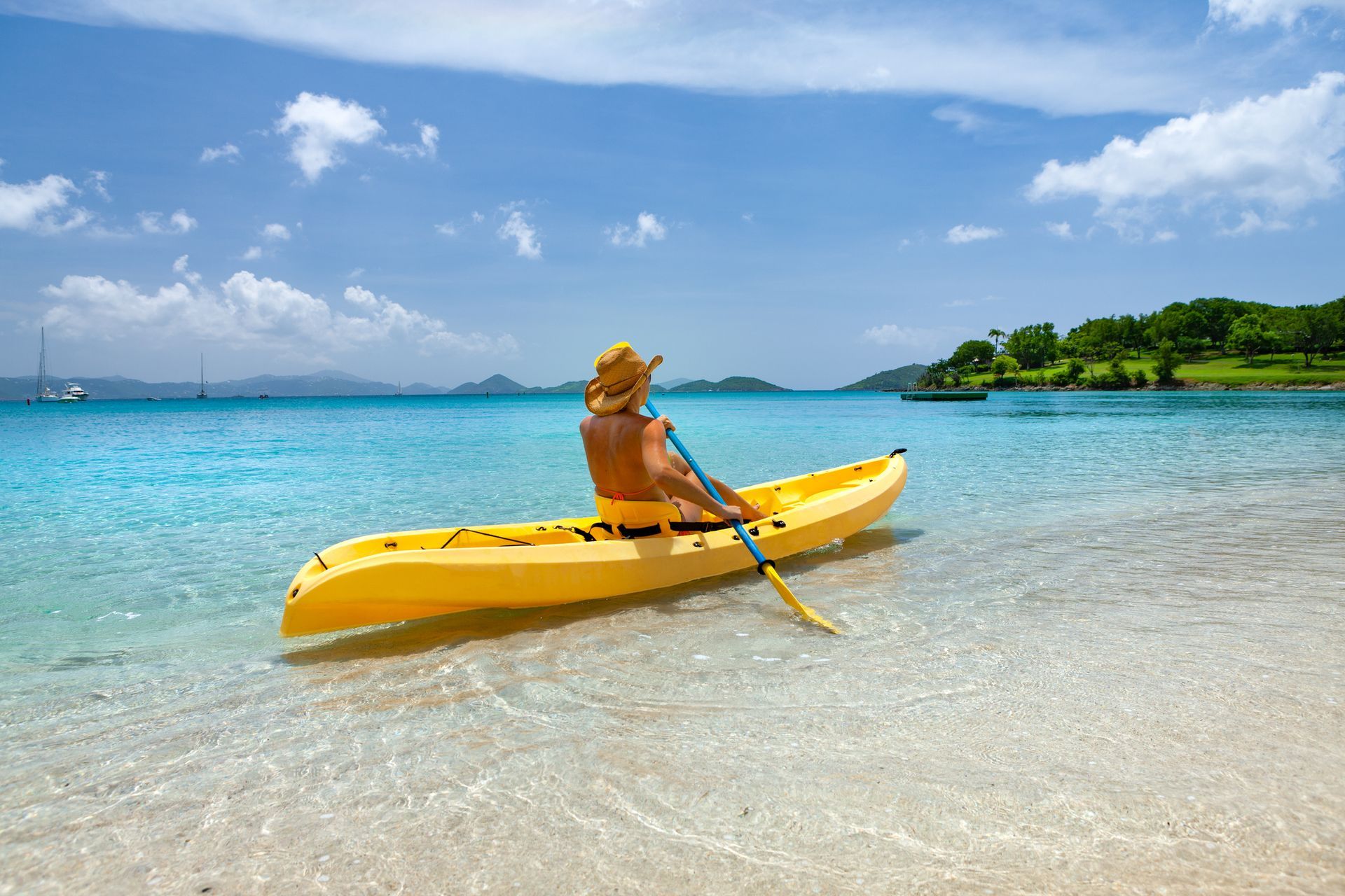 A man is sitting in a yellow kayak on the beach.