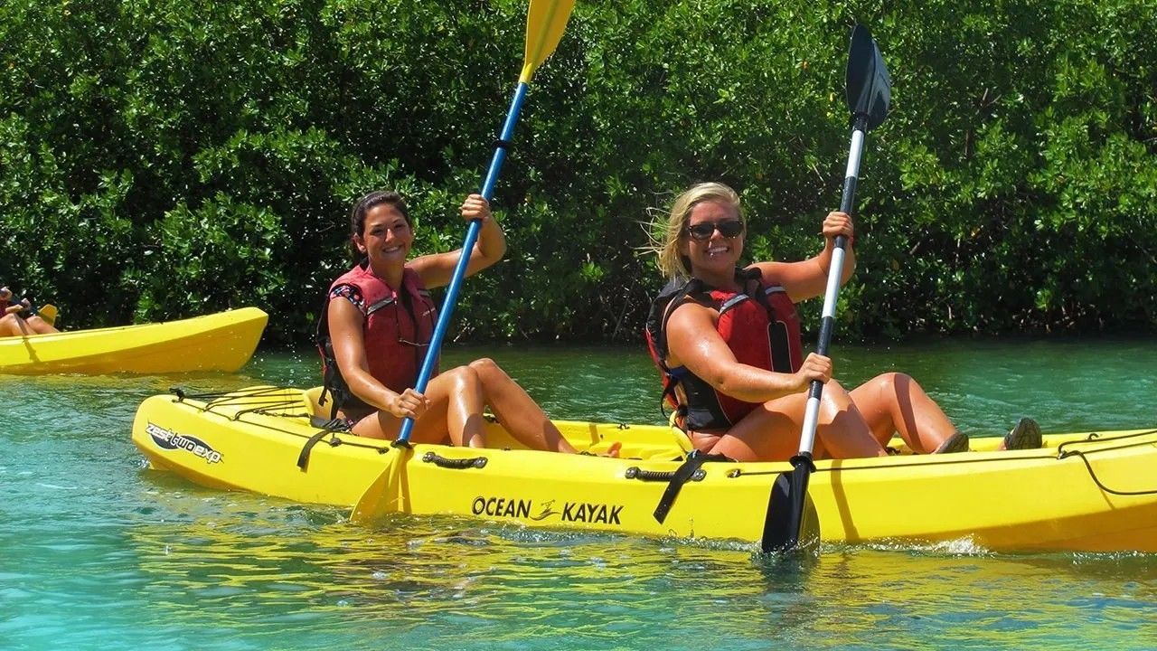 Two women are paddling yellow kayaks in the water.