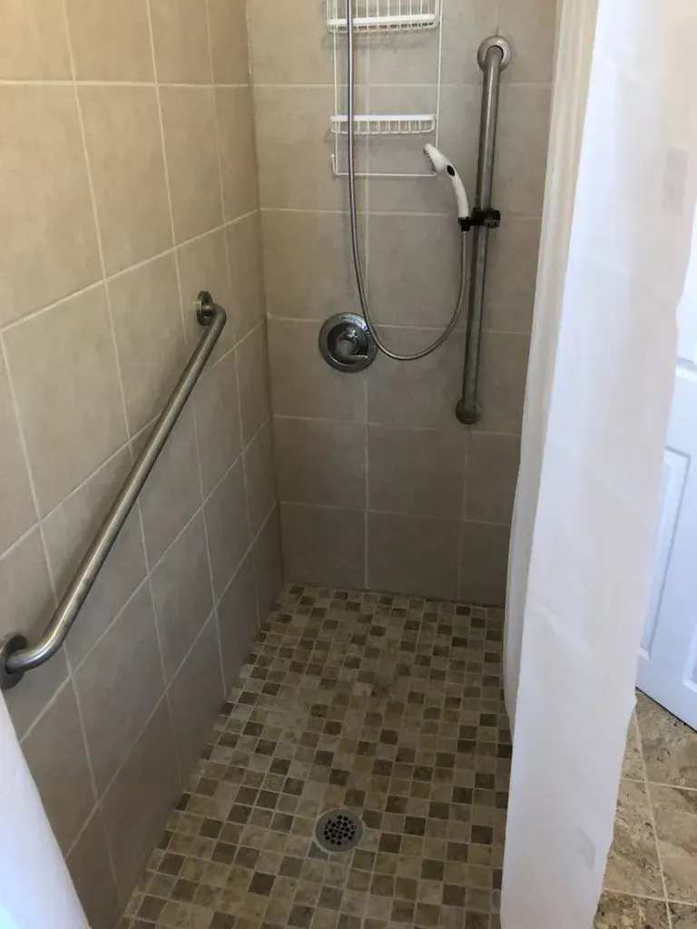 A walk in shower with a hand rail and a shower head.