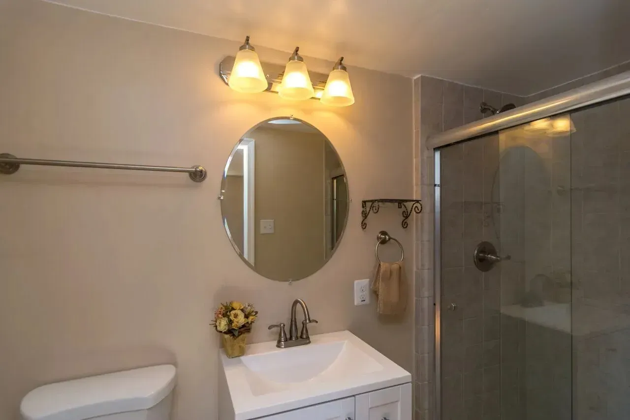 A bathroom with a toilet , sink , mirror and shower.