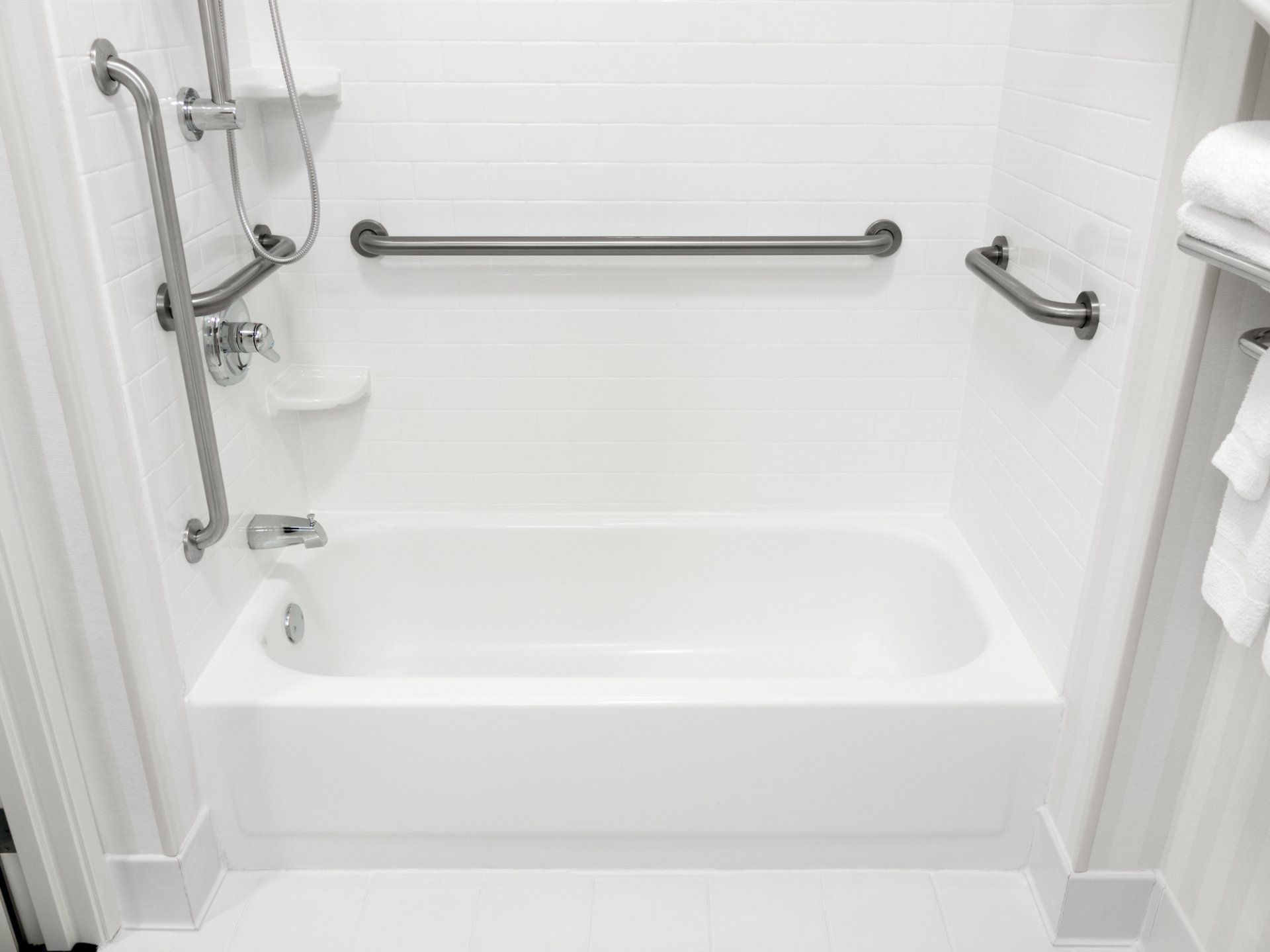 A white bathtub with stainless steel handles in a bathroom.