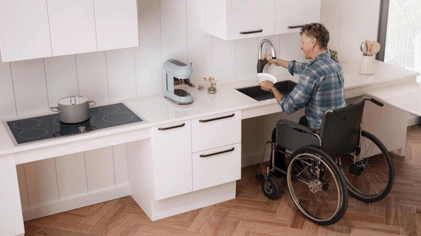 A man in a wheelchair is washing a plate in a kitchen.