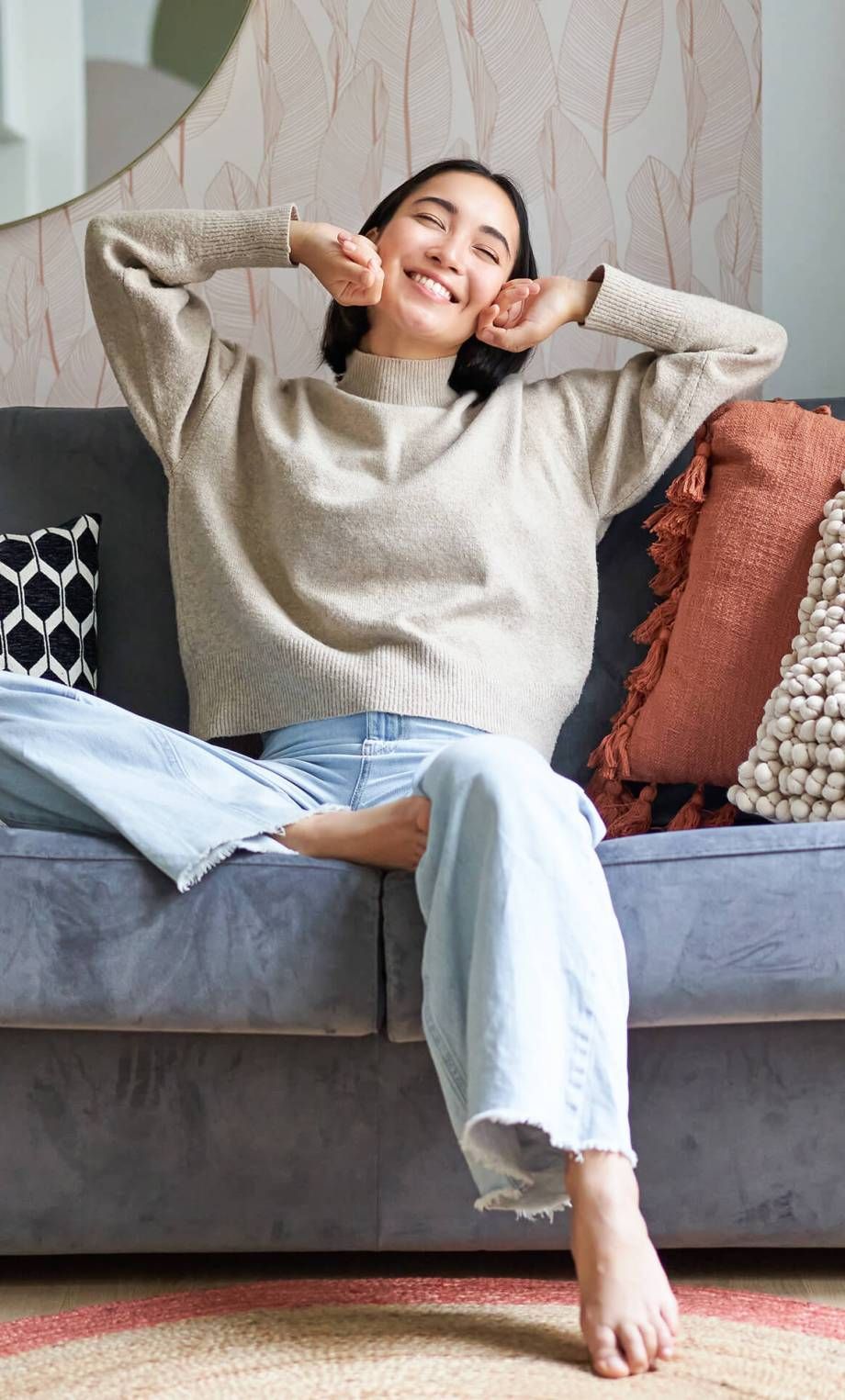 A woman is sitting on a couch with her hands behind her head.