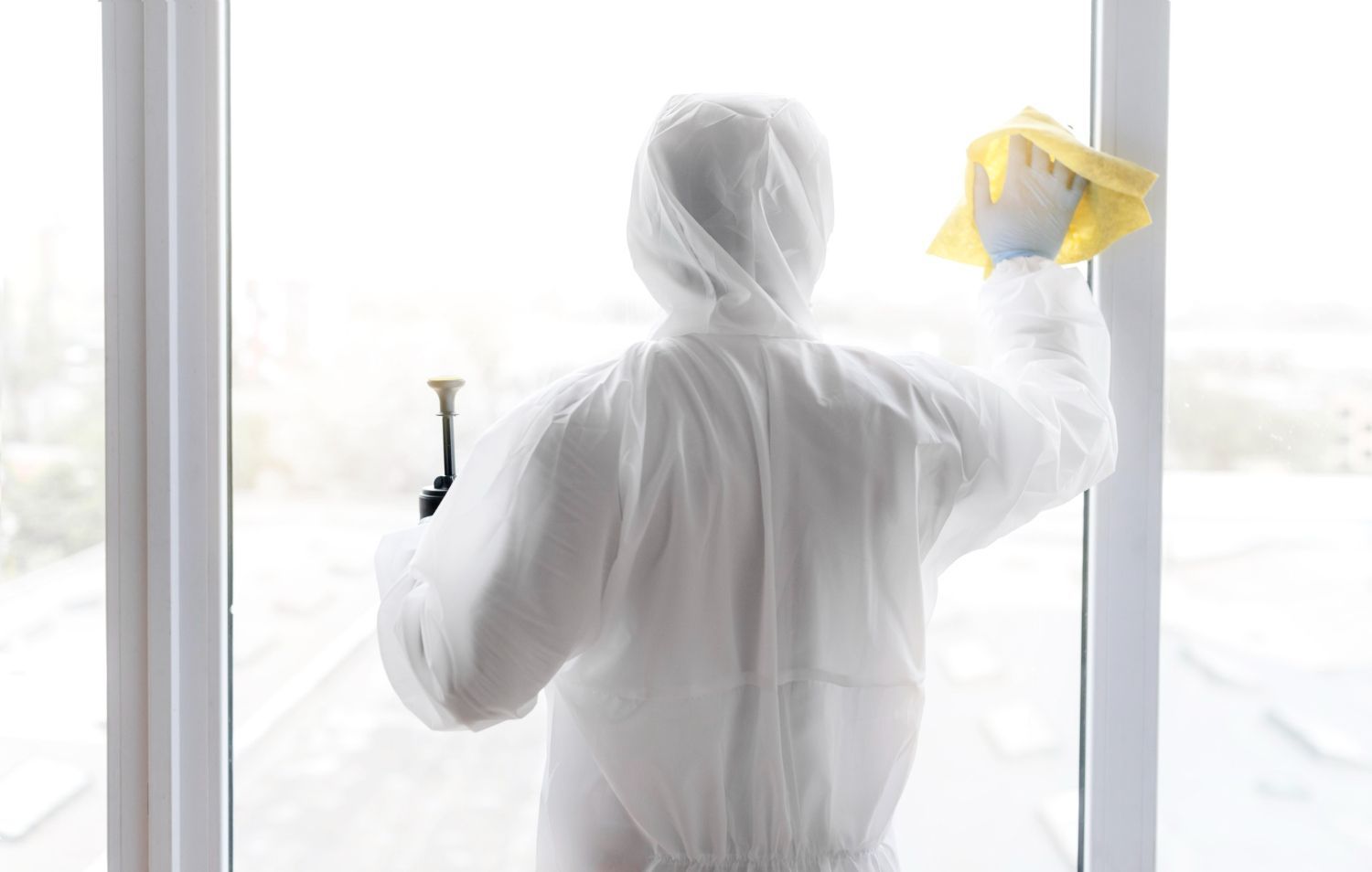 A man in a protective suit is cleaning a window with a cloth.