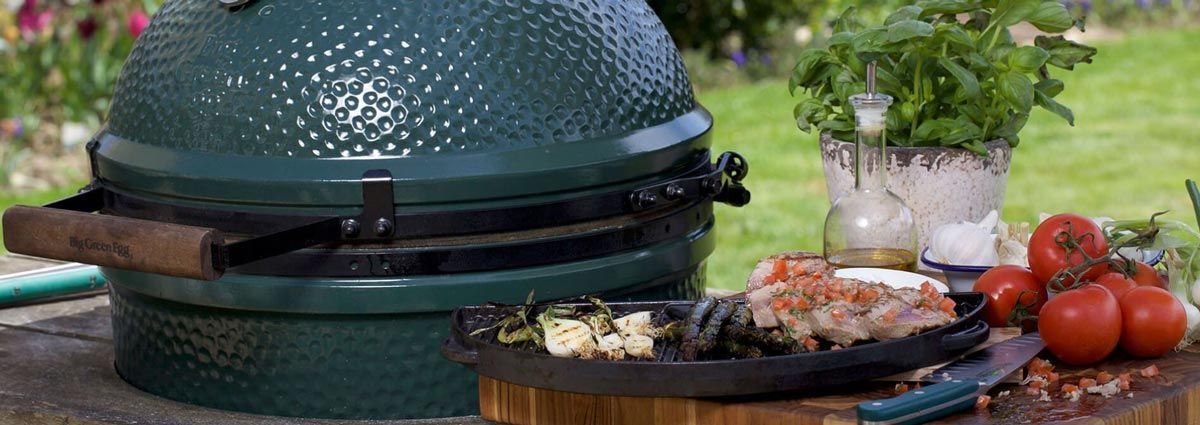 A large green egg grill is sitting on top of a wooden table.