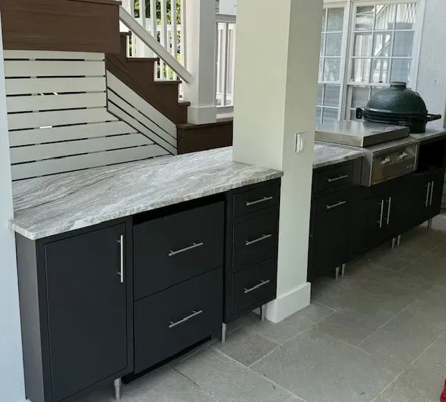 Modern kitchen/bar area with dark cabinets, white marble countertops, and gray tile floor near a staircase