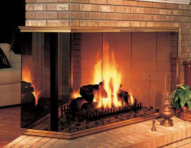 A fireplace with a glass screen surrounding it is lit up in a living room.