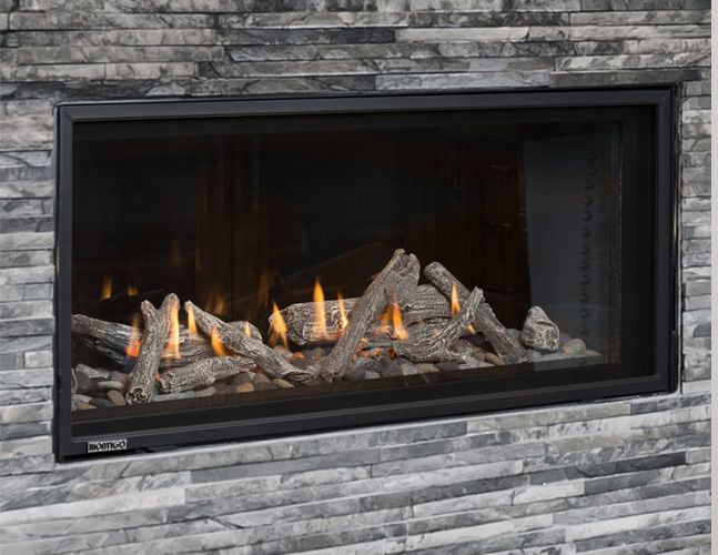 A fireplace with logs in it is built into a stone wall.