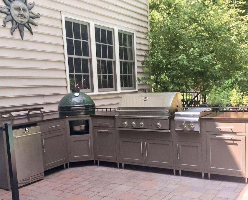 Outdoor patio with built-in grill, green dome smoker, sink, and storage cabinets under a window