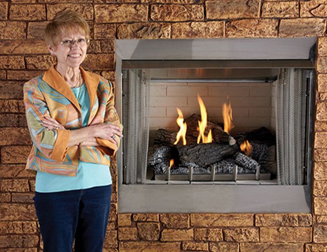 A woman is standing in front of a fireplace with her arms crossed.